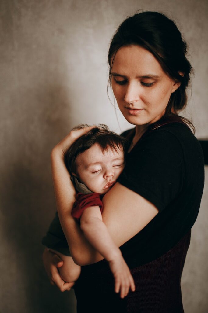 Caring mother with cute little son napping in arms standing near wall in light room during bed time at home, 7 month old sleeping