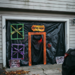 Garage door decorated for Halloween with black plastic, a faux orange doorway, and signs saying "Enter Now" and "Beware of the Dark."