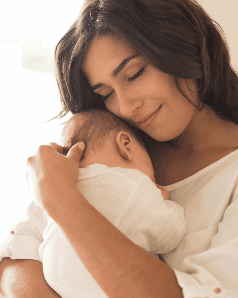A woman gently holding a baby close to her chest, both wearing white clothing, with the woman displaying a serene and loving expression.
