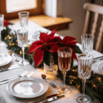 A festive dining table set with white plates, crystal glasses, and silver cutlery on a white tablecloth, decorated with red poinsettias and evergreen garlands with lights.