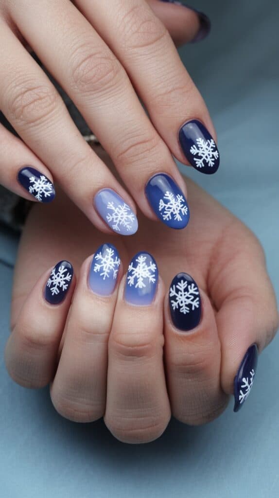 Close-up of hands with dark blue and light blue gradient nails featuring white snowflake designs on each nail.