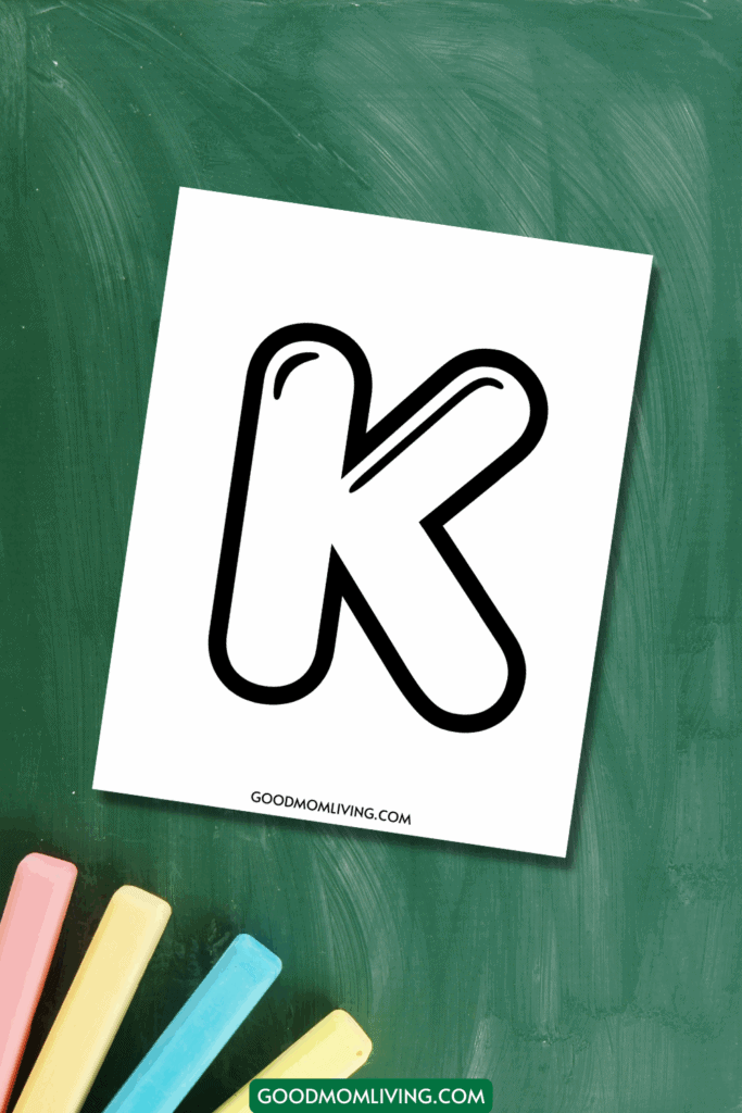 A piece of paper with a large, bold letter 'K' in a playful font on a green chalkboard background, with several colored chalk pieces at the bottom.