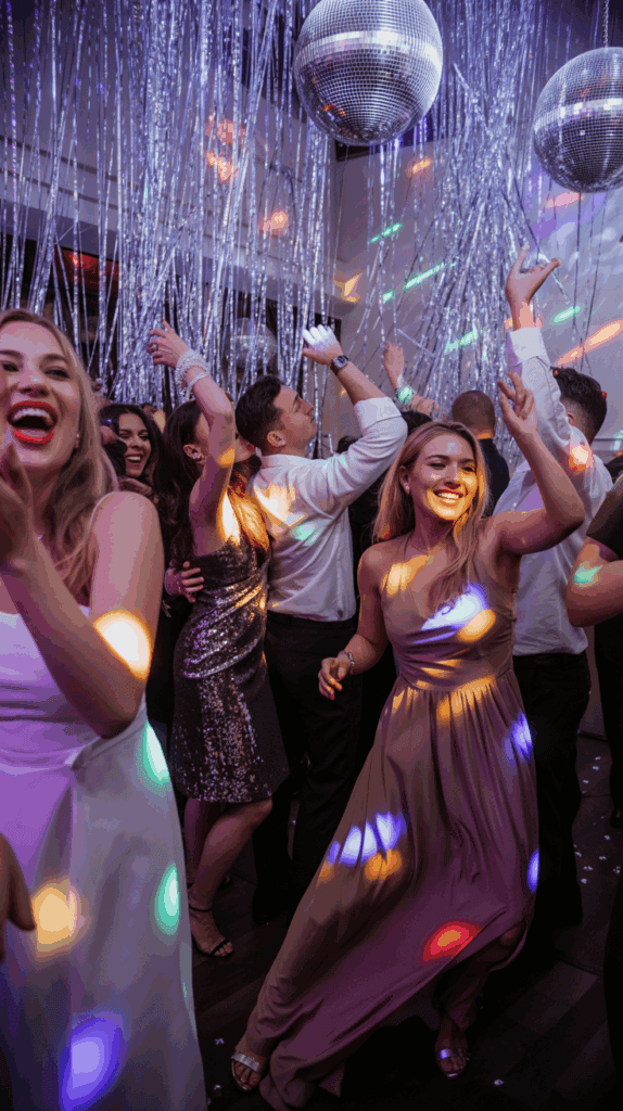 A lively dance floor with people celebrating, surrounded by shimmering streamers and disco balls reflecting colorful lights.