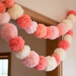 A garland of pink and cream pom-poms hangs over a wooden doorway inside a room with peach-colored walls.