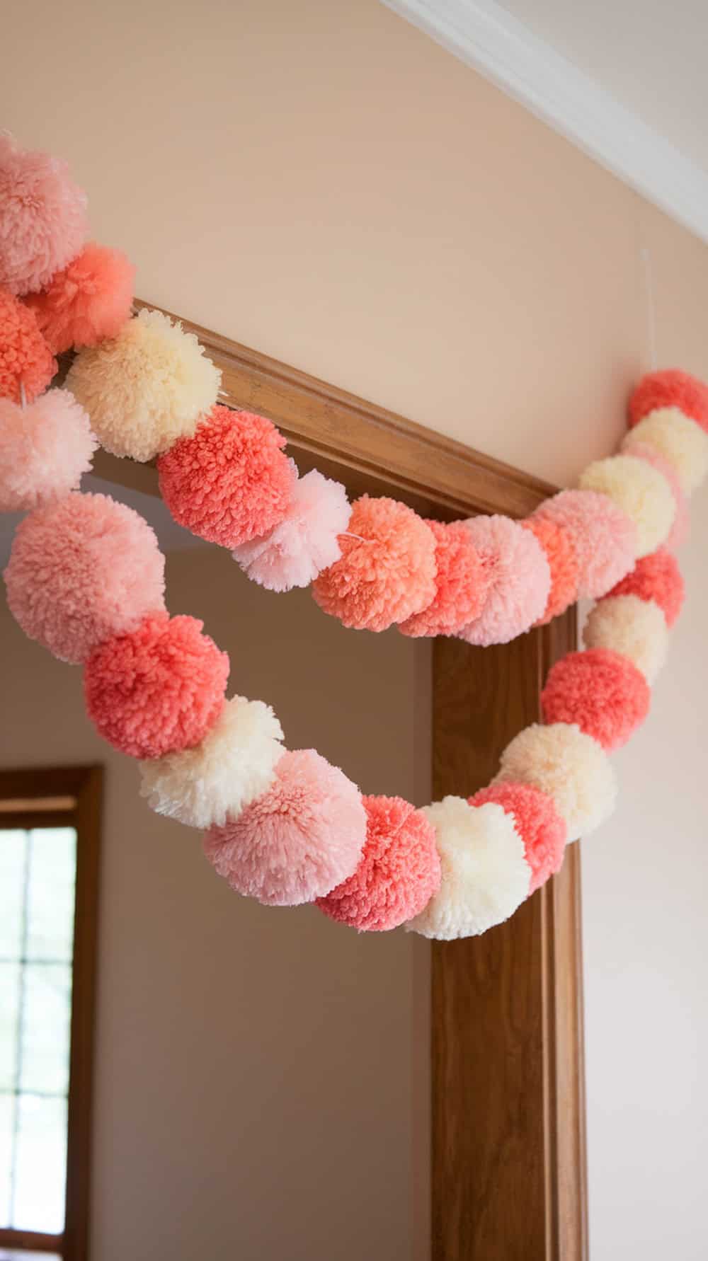A garland of pink and cream pom-poms hangs over a wooden doorway inside a room with peach-colored walls.