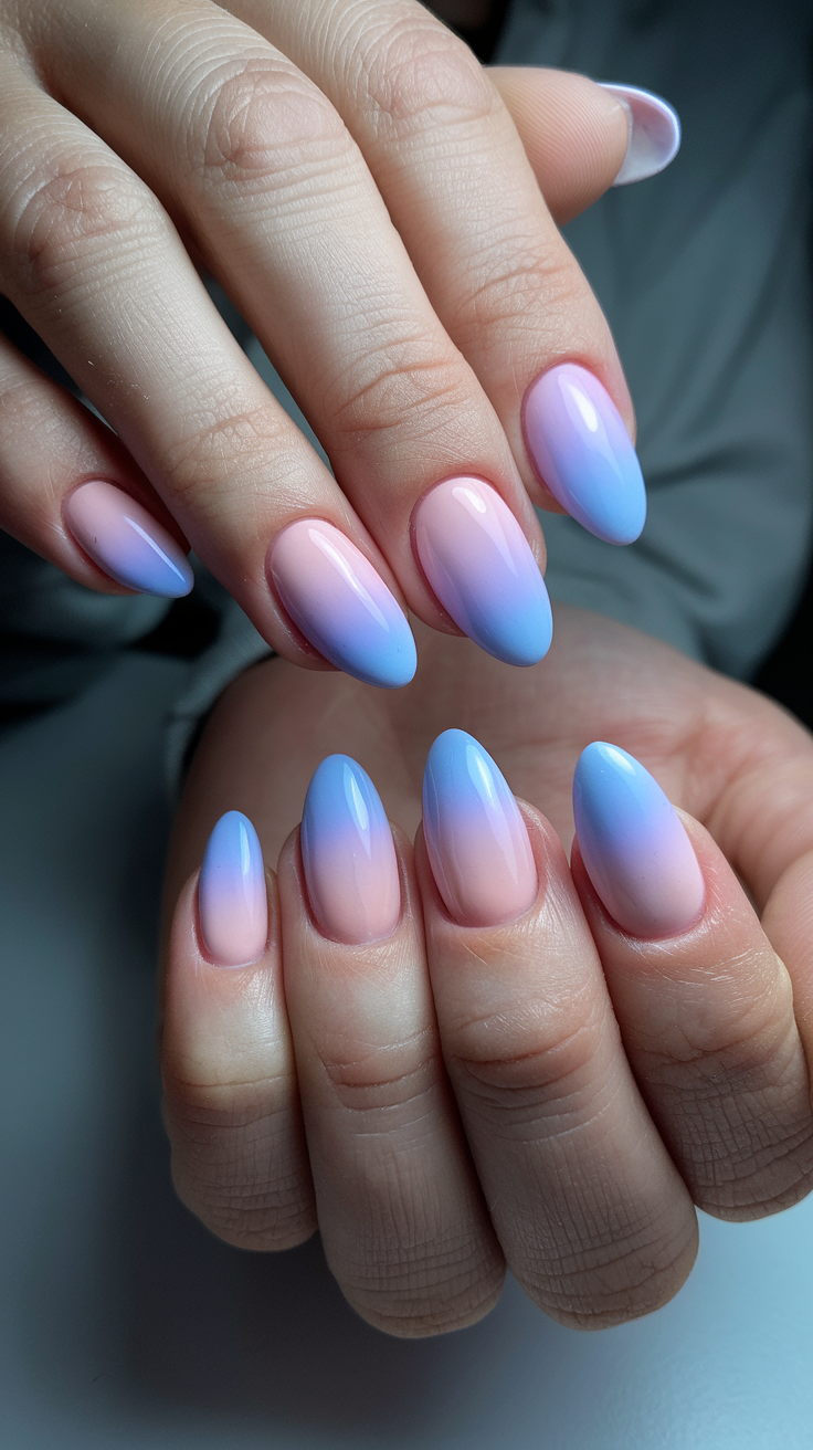 Close-up of hands displaying a manicure with an ombre effect, transitioning from pink at the base to blue at the tips on long, almond-shaped nails.