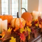 Fall-themed mantel decoration with pumpkins, colorful autumn leaves, and lit candles.