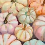 A collection of pastel-colored pumpkins, including shades of pink, blue, and cream, artistically arranged on a warm-toned surface with leaves scattered around.