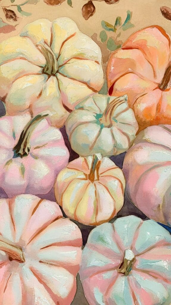 A collection of pastel-colored pumpkins, including shades of pink, blue, and cream, artistically arranged on a warm-toned surface with leaves scattered around.